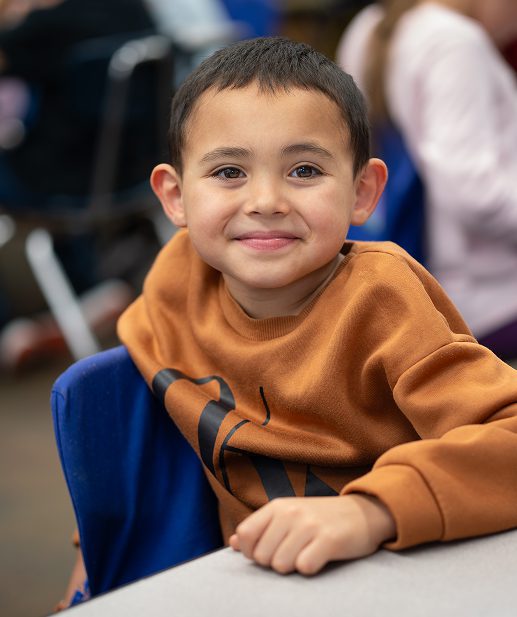 A BARR student wearing an orange shirt sitting in a chair and smiling